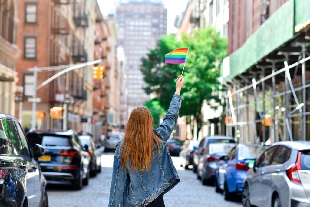 Vibrant LGBTQ-Friendly Cities for Travel Assignments Woman holding a rainbow Pride flag in New York City, showing LGBTQ+ pride and visibility in an urban setting.