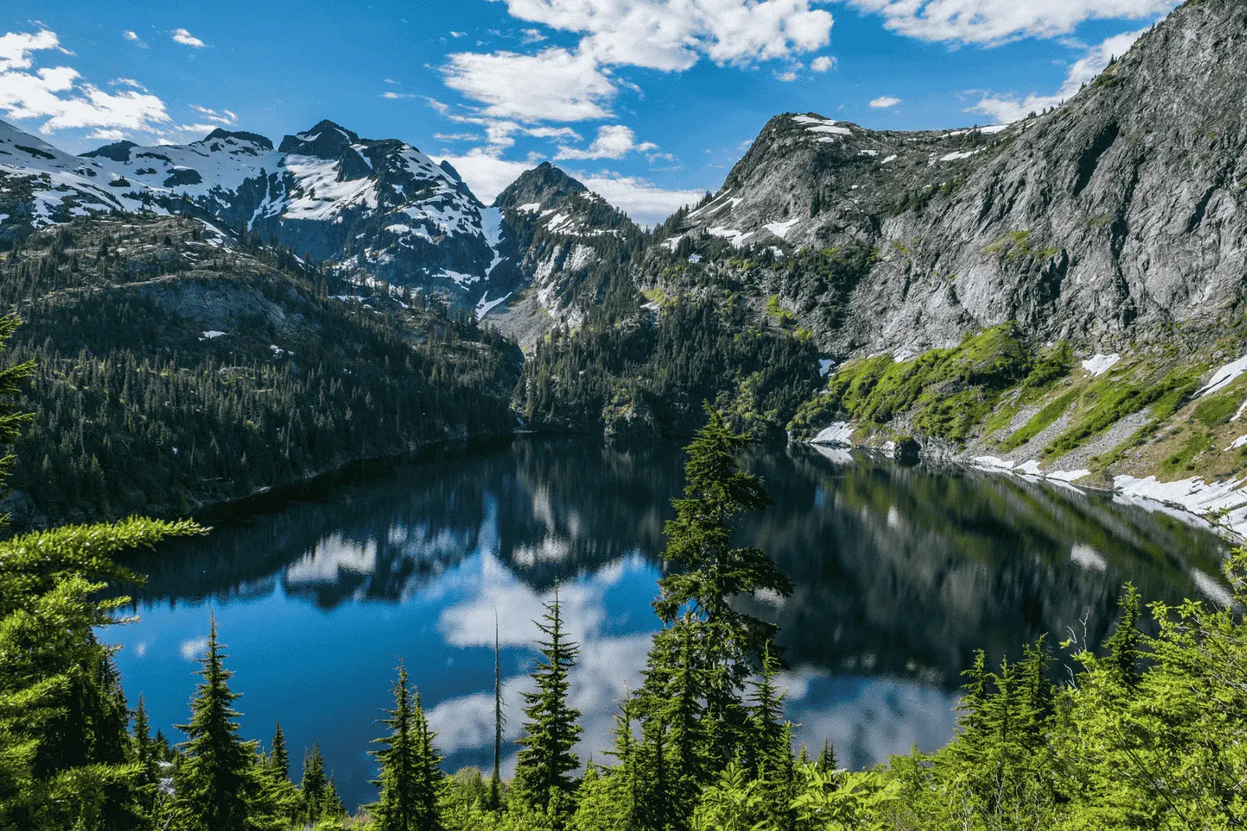 5 Mountainous National Parks and Top Hikes for the Best Views view of snowcapped mountains with a lake below surrounded by trees